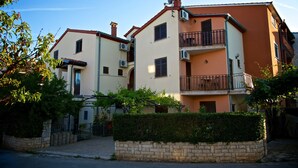 A multi-story residential building with balconies, air conditioning units, and a stone wall in front. - Apartmani Exclusive (Rovinj)