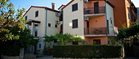 A multi-story residential building with balconies, air conditioning units, and a stone wall in front.