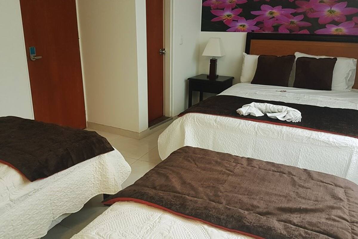 A hotel room with two beds, each with a brown blanket and white bedding. There is a nightstand with a lamp and a wall with a floral wallpaper.