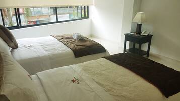 A hotel room with two beds, a nightstand with a lamp, and a window with a view of the outside.