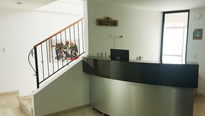 Una recepción con una barandilla metálica, un letrero de salida/entrada y una ventana con persianas.