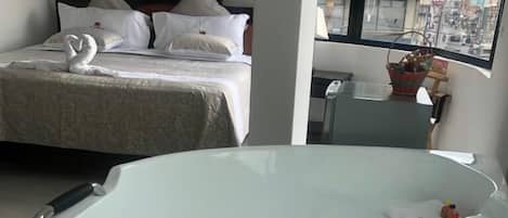 A modern hotel room with a large bathtub, a neatly made bed, and a window with a city view.