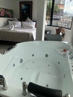 Una habitación de hotel moderna con una bañera grande, una cama bien hecha y un ventanal con vistas a la ciudad.