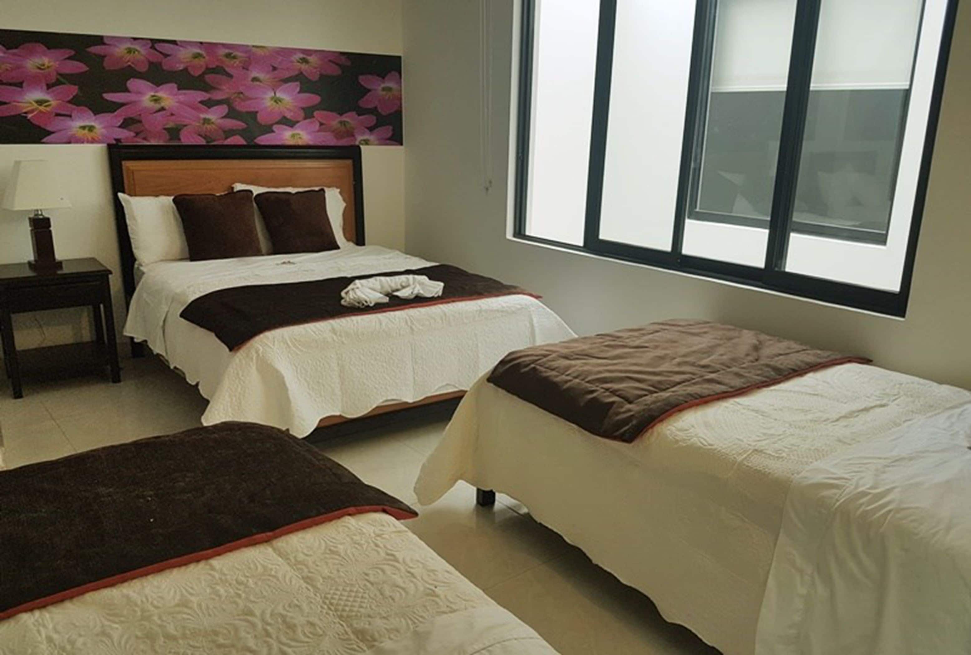 A hotel room with two beds, a nightstand, a window, and a floral wall decoration.