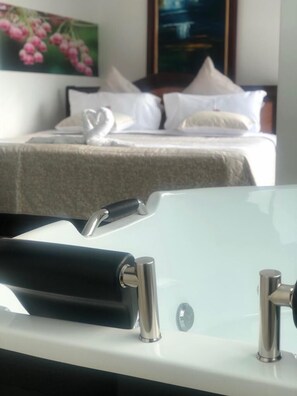 A bathroom with a modern sink and a bed with white bedding and swan-shaped pillows in the background. - Hotel Santa Monica (Fusagasugá)