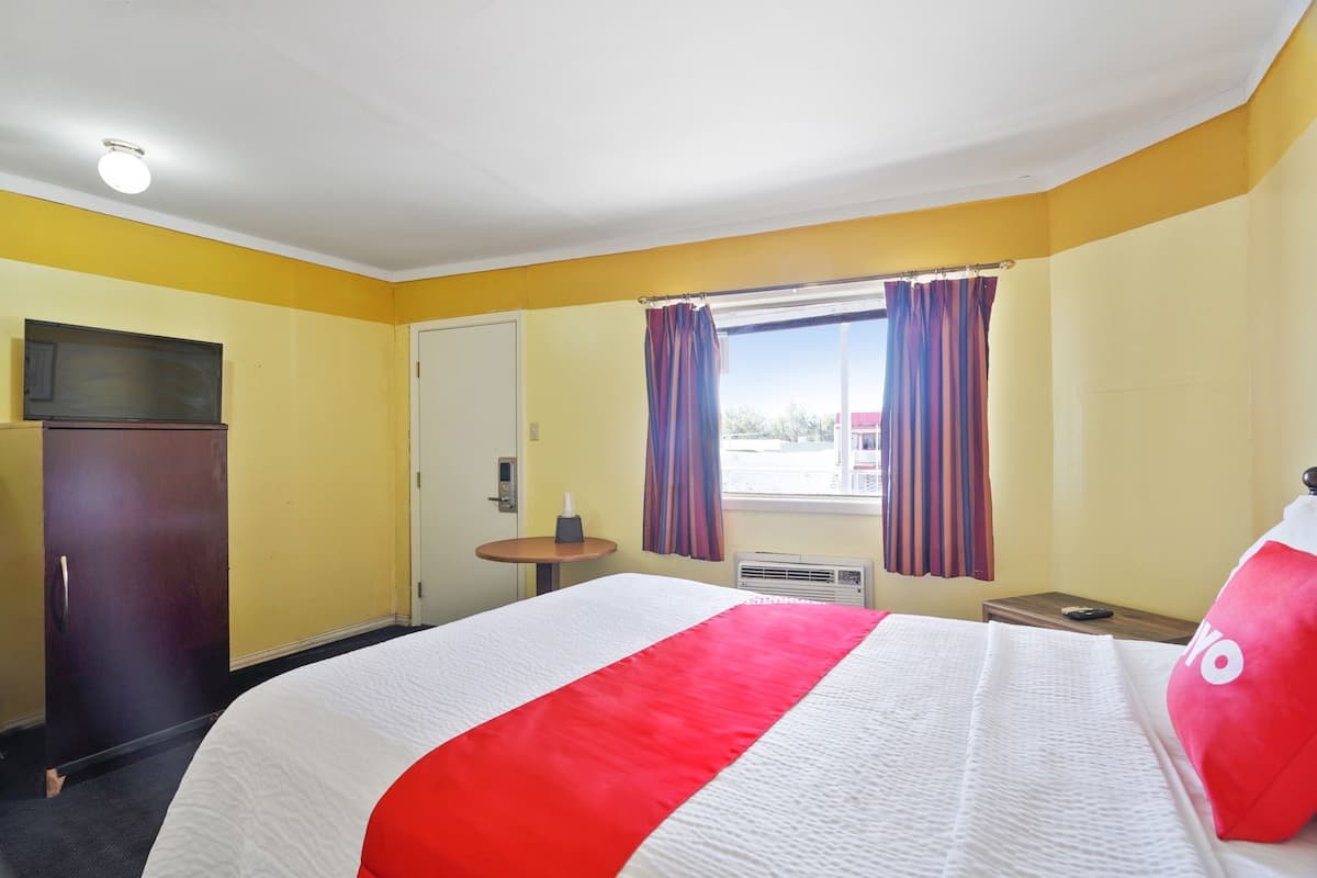 Ein Hotelzimmer mit Bett, Schreibtisch, Stuhl, Fernseher und einem Fenster mit Vorhängen.