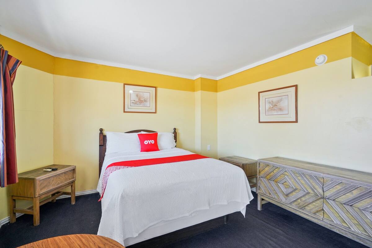 Ein Hotelzimmer mit Bett, Nachttisch, Kommode und zwei gerahmten Bildern an der Wand.