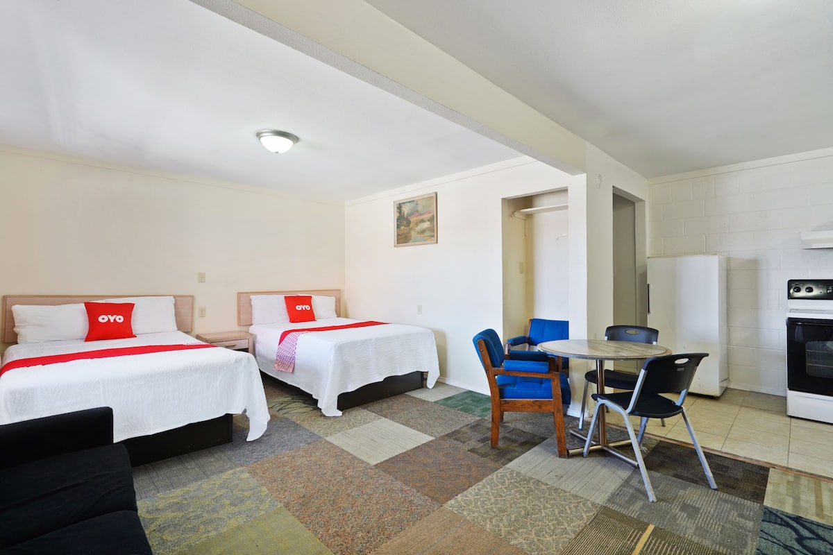 Ein Hotelzimmer mit zwei Betten, einem kleinen Esstisch mit Stühlen, einer Küchenzeile und Teppichboden.