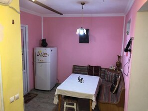 A compact kitchen with a refrigerator, a table with a checkered tablecloth, and a patterned sofa. - Guest House Nise (Tbilisi)