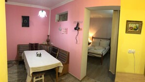 A room with a pink wall, a bed with a white headboard, a table with a checkered tablecloth, and a lamp on the wall. - Guest House Nise (Tbilisi)