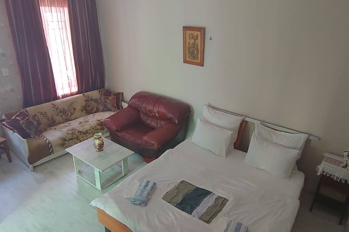 A room with a bed, a sofa, a small table, and a nightstand.