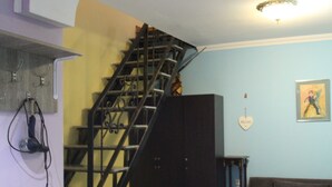 A staircase with a metal railing leading to a landing, a brown sofa, a patterned ottoman, and a small wooden stool. - Guest House Nise (Tbilisi)