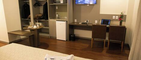 A hotel room with a bed, a desk with a laptop, a TV, a microwave, and a mini-fridge.