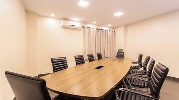 A conference room with a long wooden table, black leather chairs, and a white air conditioning unit on the wall.