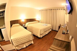 A hotel room with two beds, a desk, a television, and a small kitchenette.