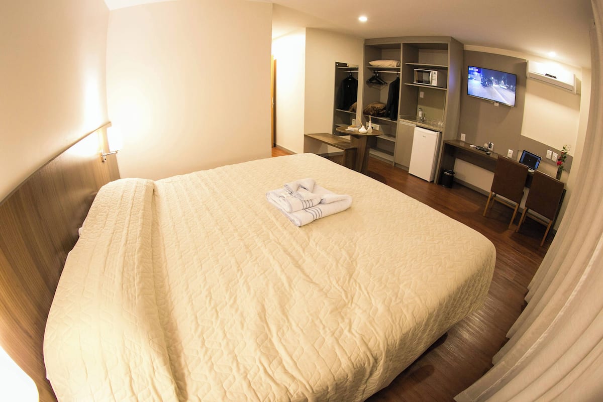 A hotel room with a large bed, a desk, a television, and a wardrobe.