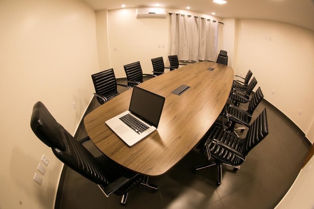 Een vergaderruimte met een lange tafel, zwarte stoelen en een laptop op tafel.