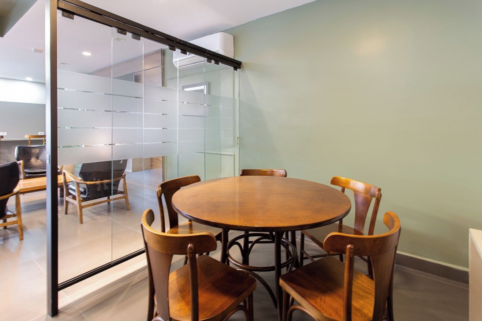 Un salón de conferencias con una mesa redonda y seis sillas de madera, un separador de vidrio y una puerta corrediza.