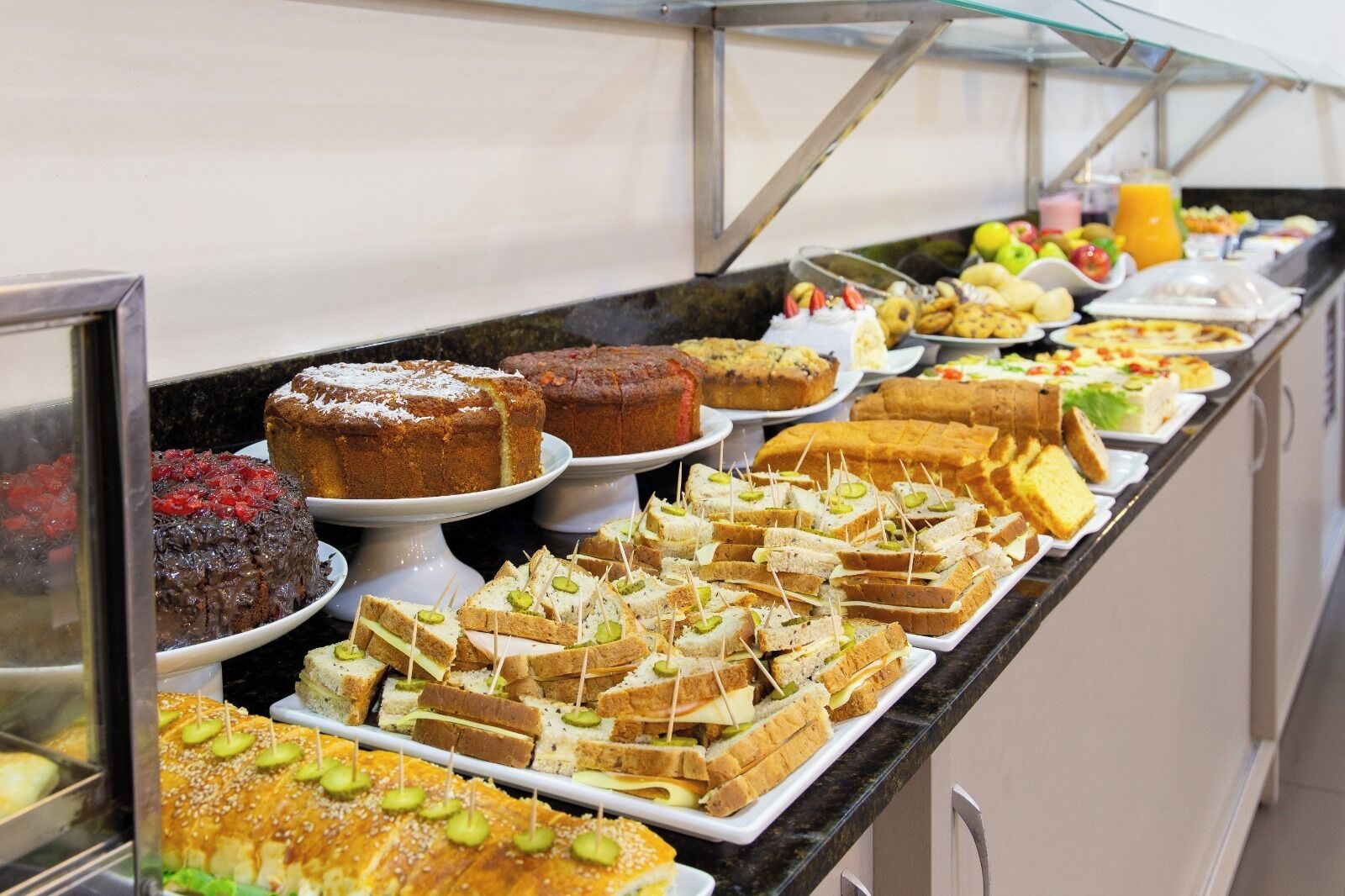 Buffet com diversas opções de comida, incluindo bolos, sanduíches e frutas.