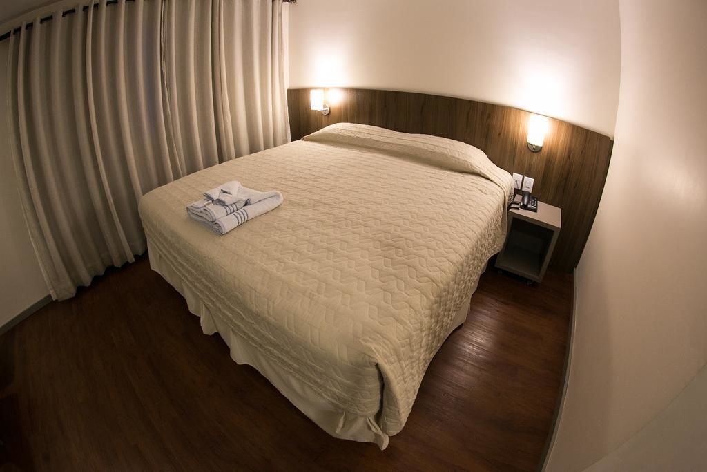 A hotel room with a large bed, a nightstand with a lamp, and a window with curtains.
