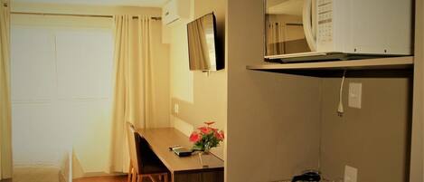 A hotel room with a wooden desk, a television, a microwave, and a small kitchenette.