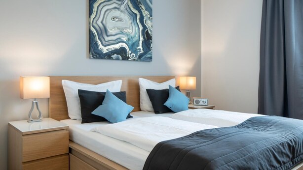 A modern hotel room with a wooden headboard, two beds, a nightstand with a lamp, a radio, and a large abstract painting on the wall. - Hotel Birkenstern (Bad Wildungen)
