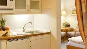 A compact kitchen with a microwave, sink, and cabinets. There's a dining area with a table and chairs, and a bed in the background. - Hotel Birkenstern (Bad Wildungen)