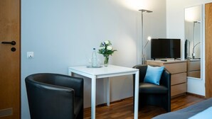 A modern hotel room with a white desk, two black chairs, a grey sofa, a TV, and a mirror. - Hotel Birkenstern (Bad Wildungen)