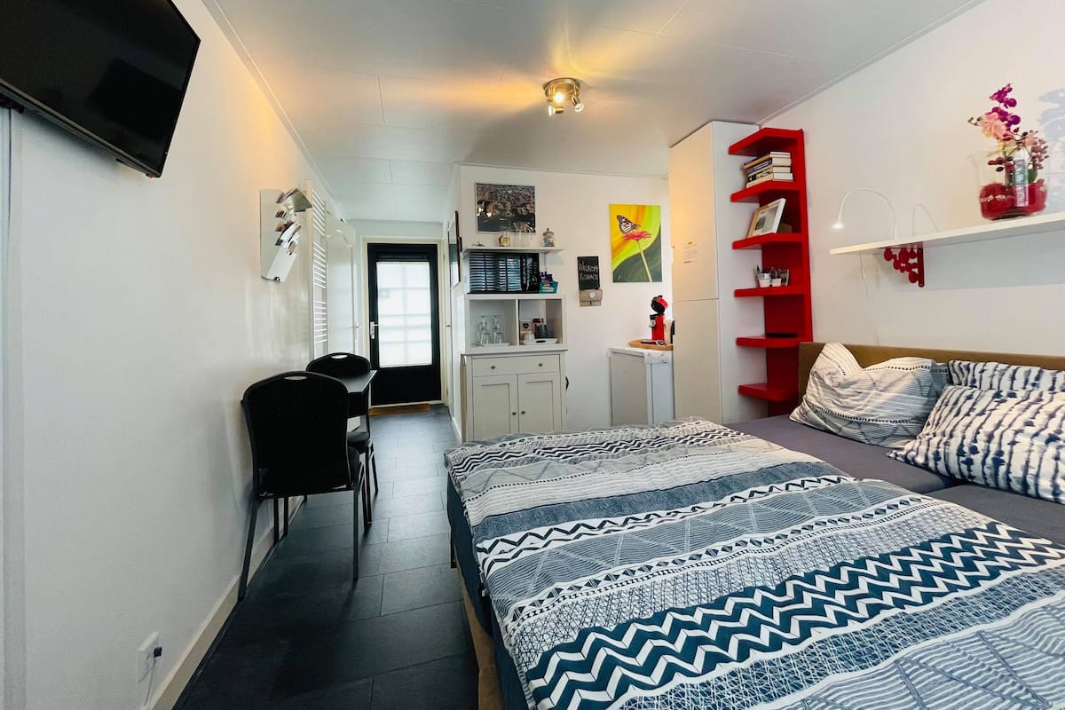 Un dormitorio con cama, escritorio, silla, armario, estantería roja y televisor.