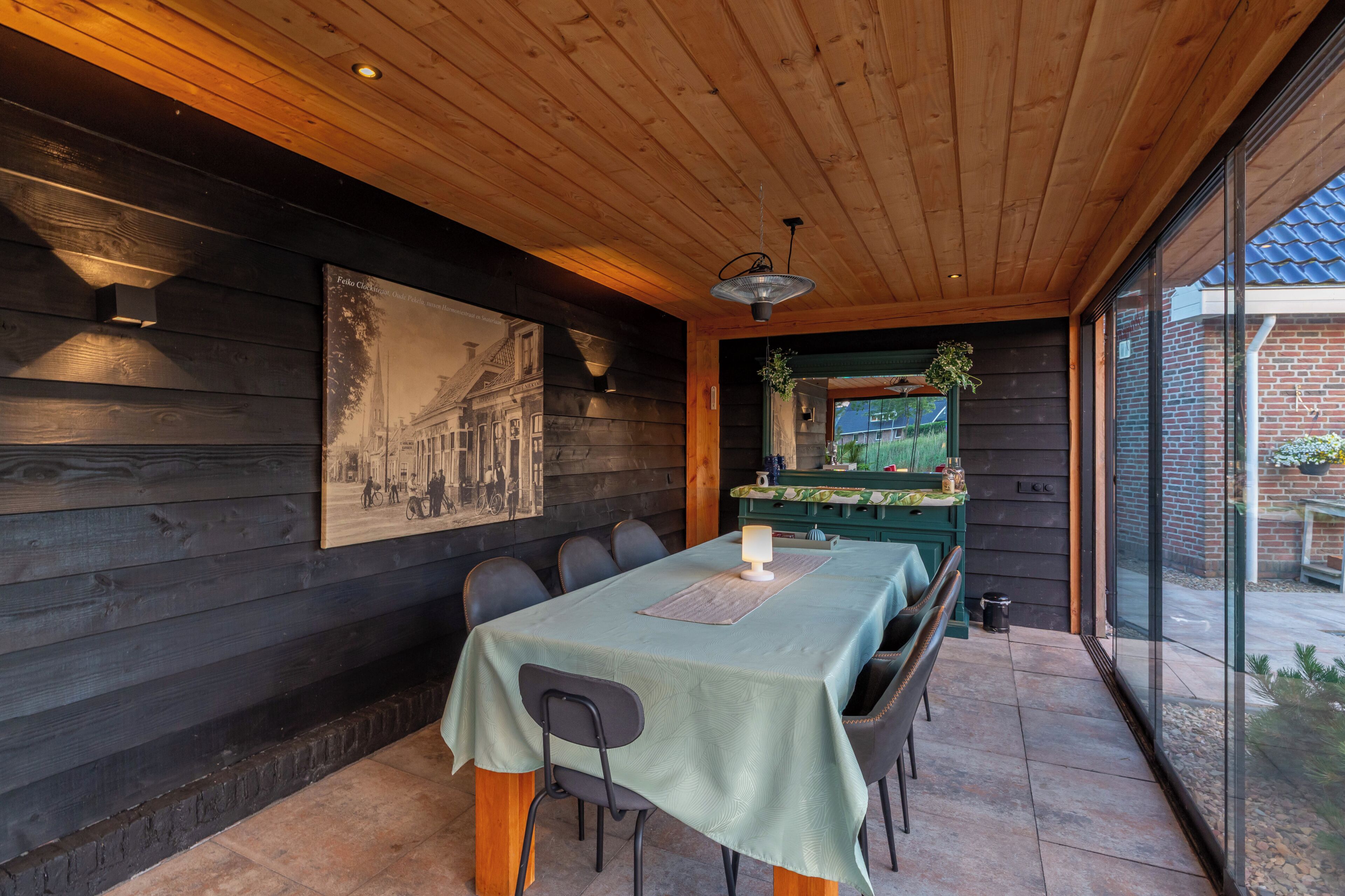 Un comedor con una mesa dispuesta para cuatro personas, paredes de madera, una lámpara colgante y un cuadro grande en la pared.