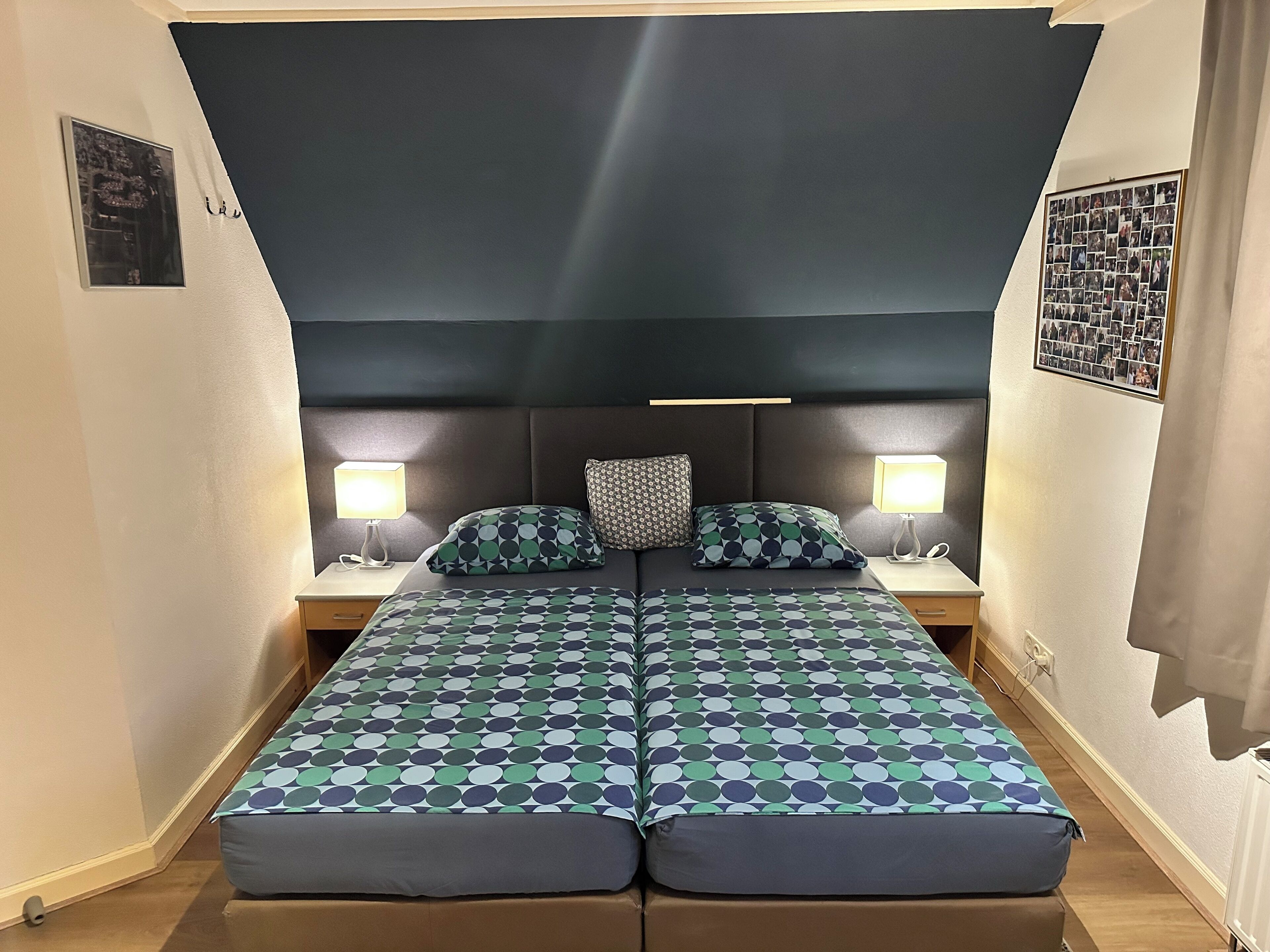 Een tweepersoonsbed met een bedspread met een geometrisch patroon, twee nachtkastjes met lampen en een donker hoofdbord.