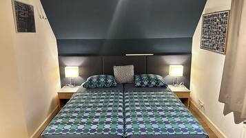 Een tweepersoonsbed met een bedspread met een geometrisch patroon, twee nachtkastjes met lampen en een donker hoofdbord.