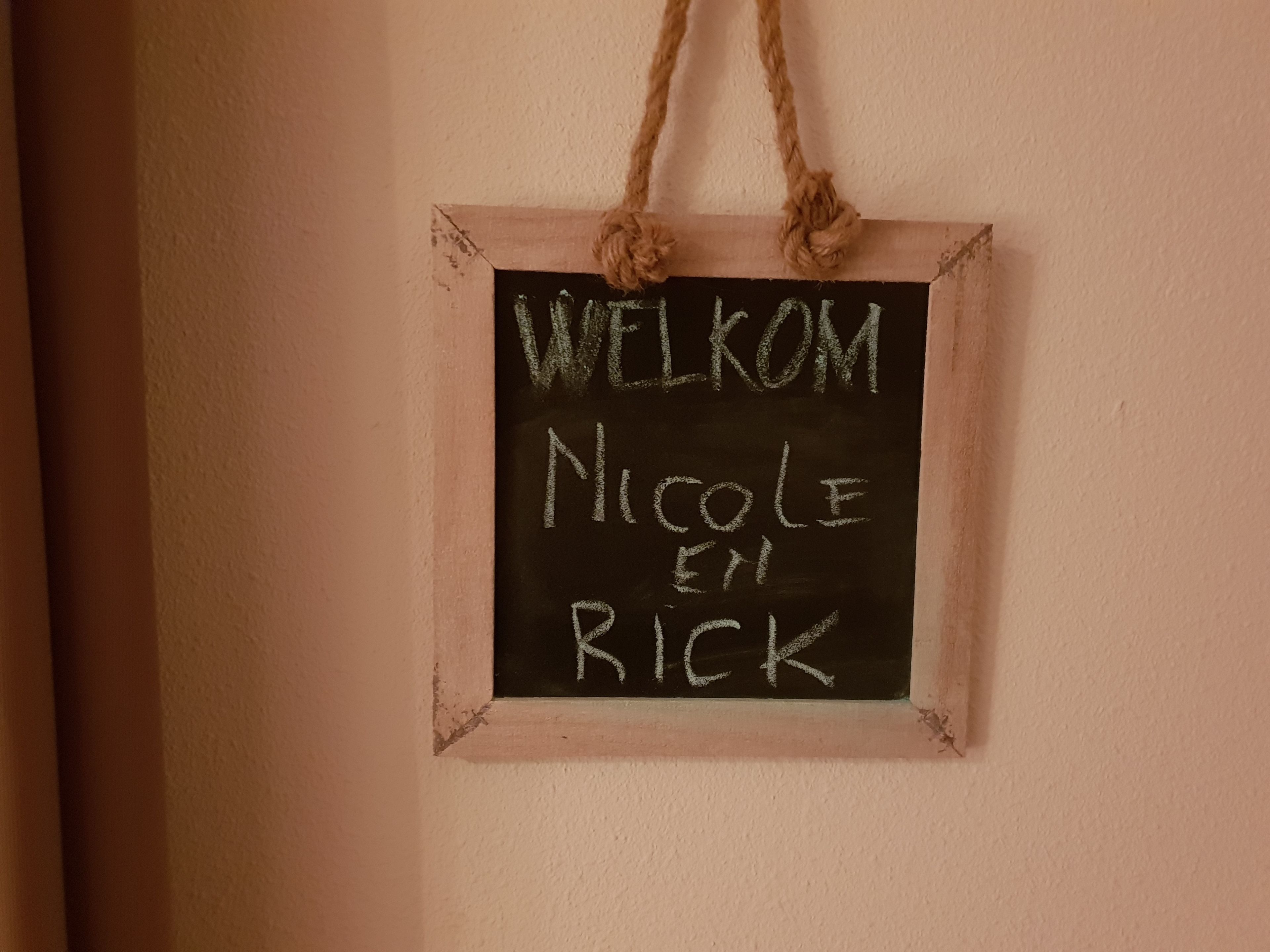 A chalkboard sign with the words "WELCOME Nicole en Rick" hanging on a wall.