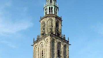 Ein historischer Turm mit einer Uhr, umgeben von einem Platz mit Außenbestuhlung und Fahrrädern.