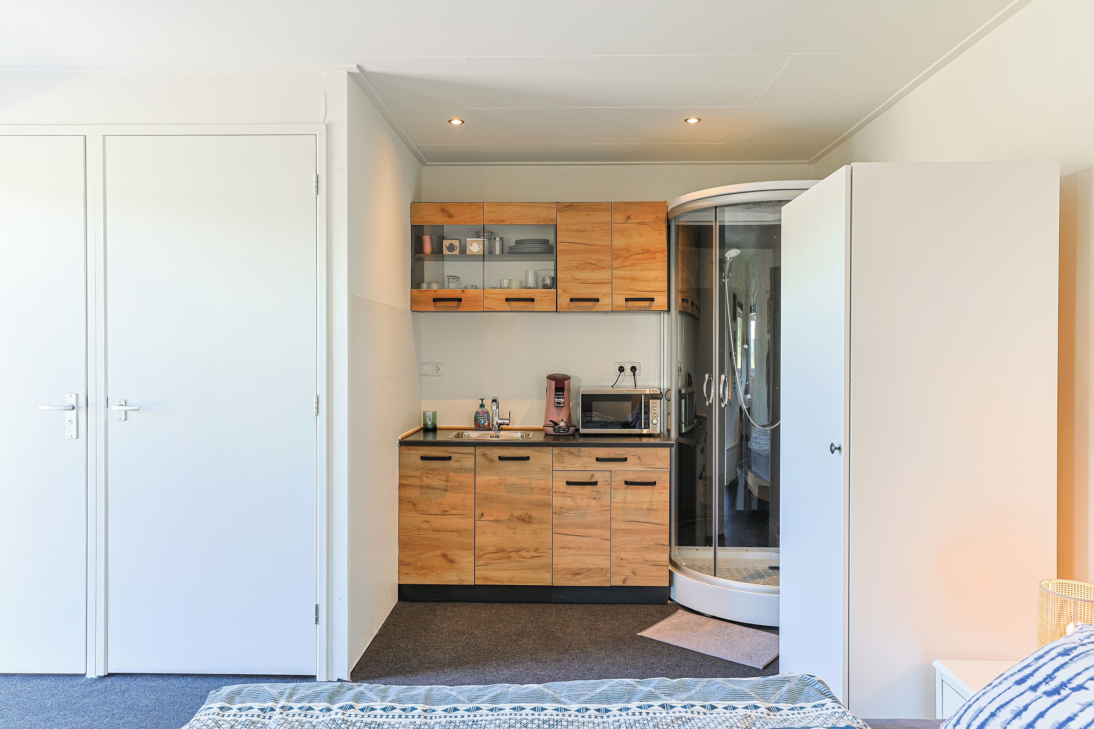 Una cocina compacta con muebles de madera, microondas y cabina de ducha de vidrio.