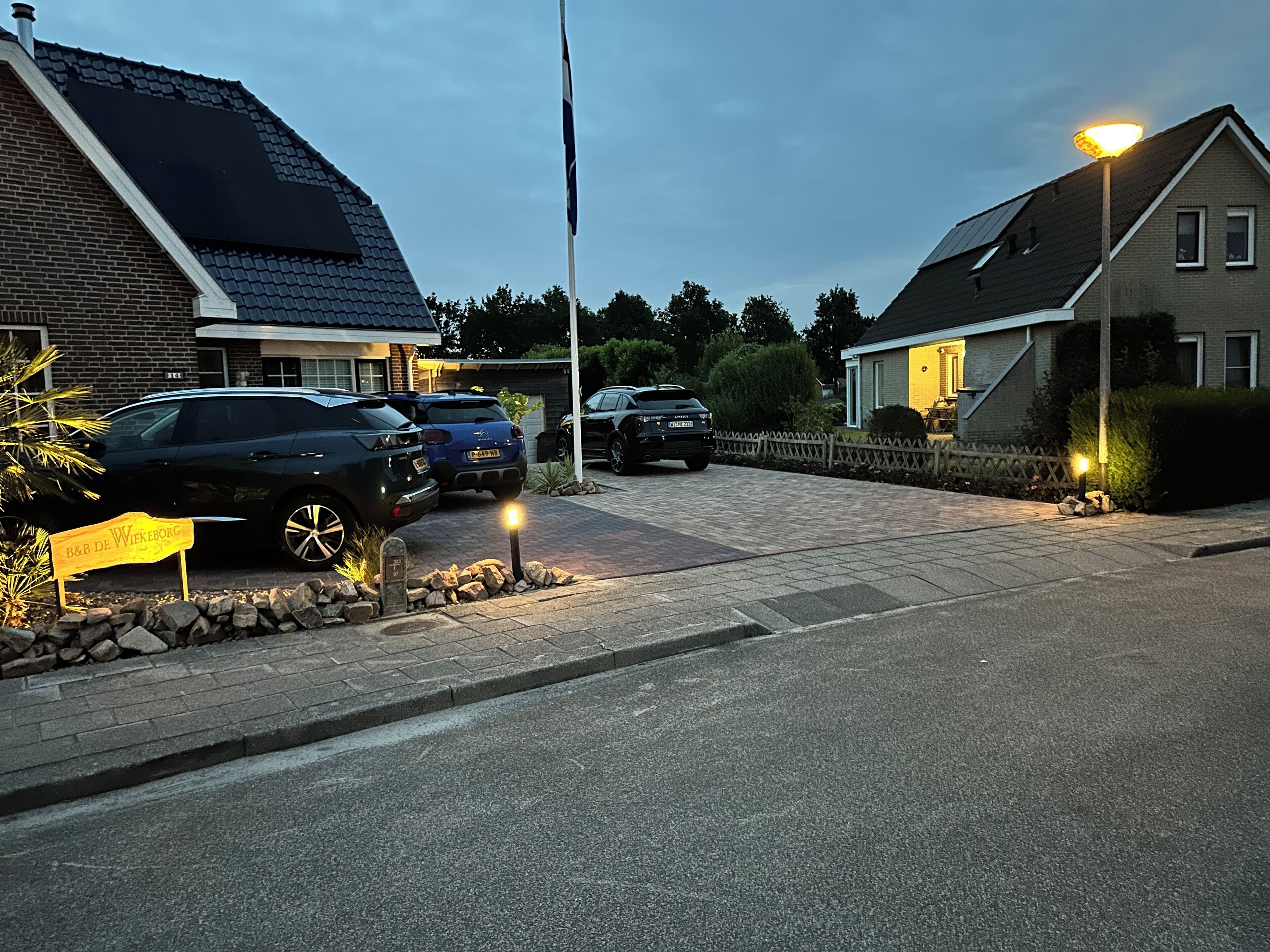 Een woonstraat met geparkeerde auto's, een stenen muur en een bordje voor B&B De Wiekeborg.