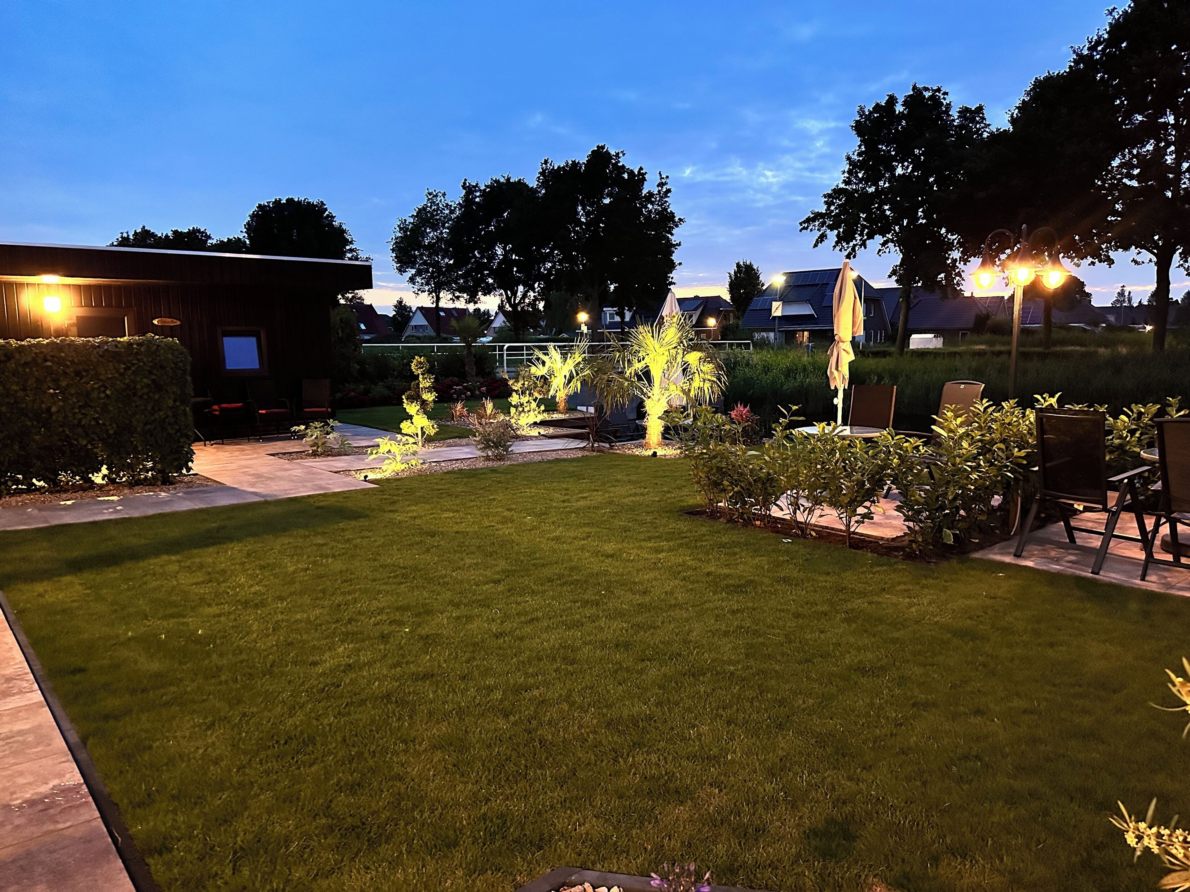 A well-maintained outdoor area with a grassy lawn, seating arrangements, and illuminated plants.