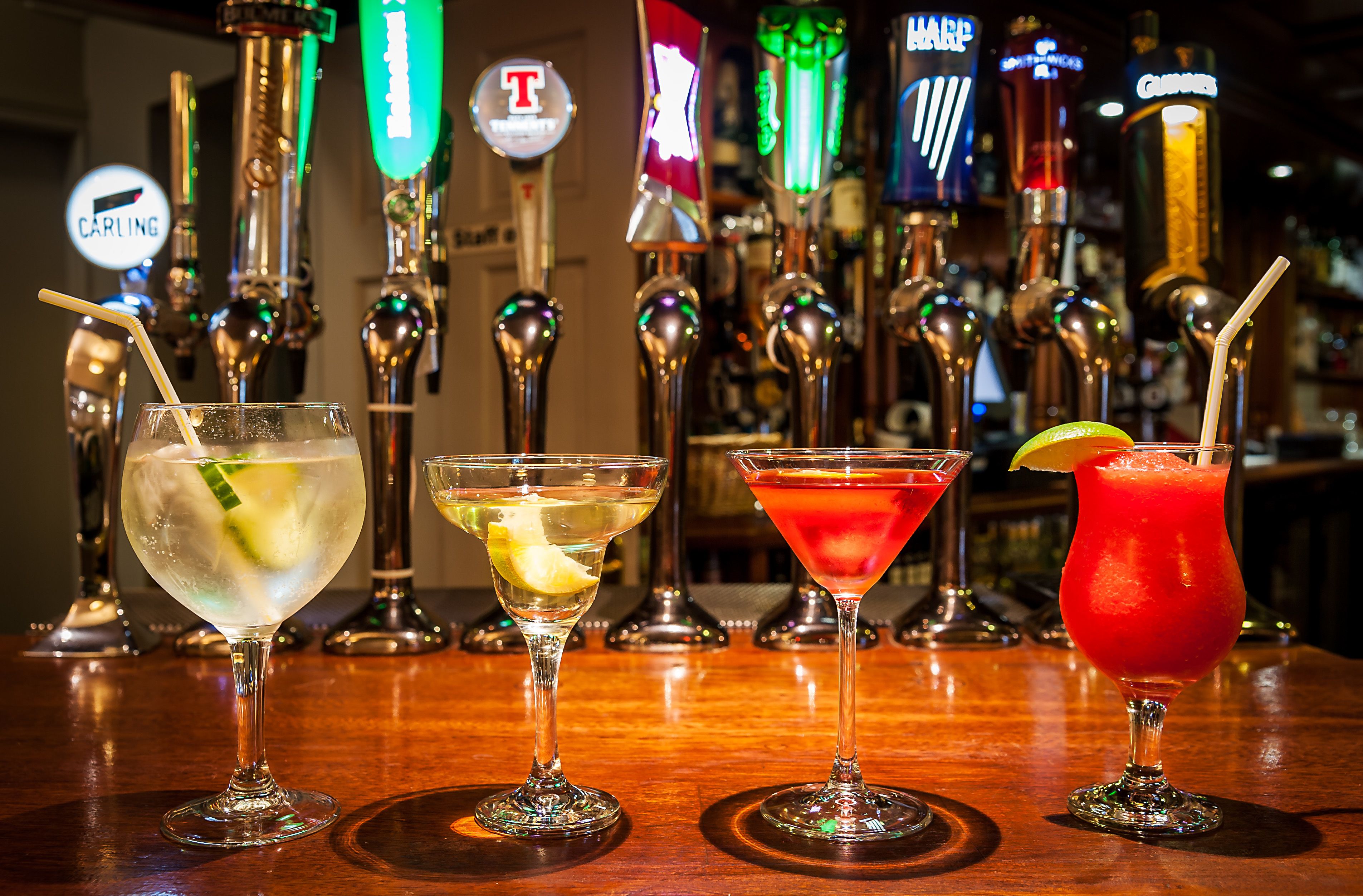 Un bar où l’on propose quatre cocktails différents, devant une rangée de robinets à bière illuminés.