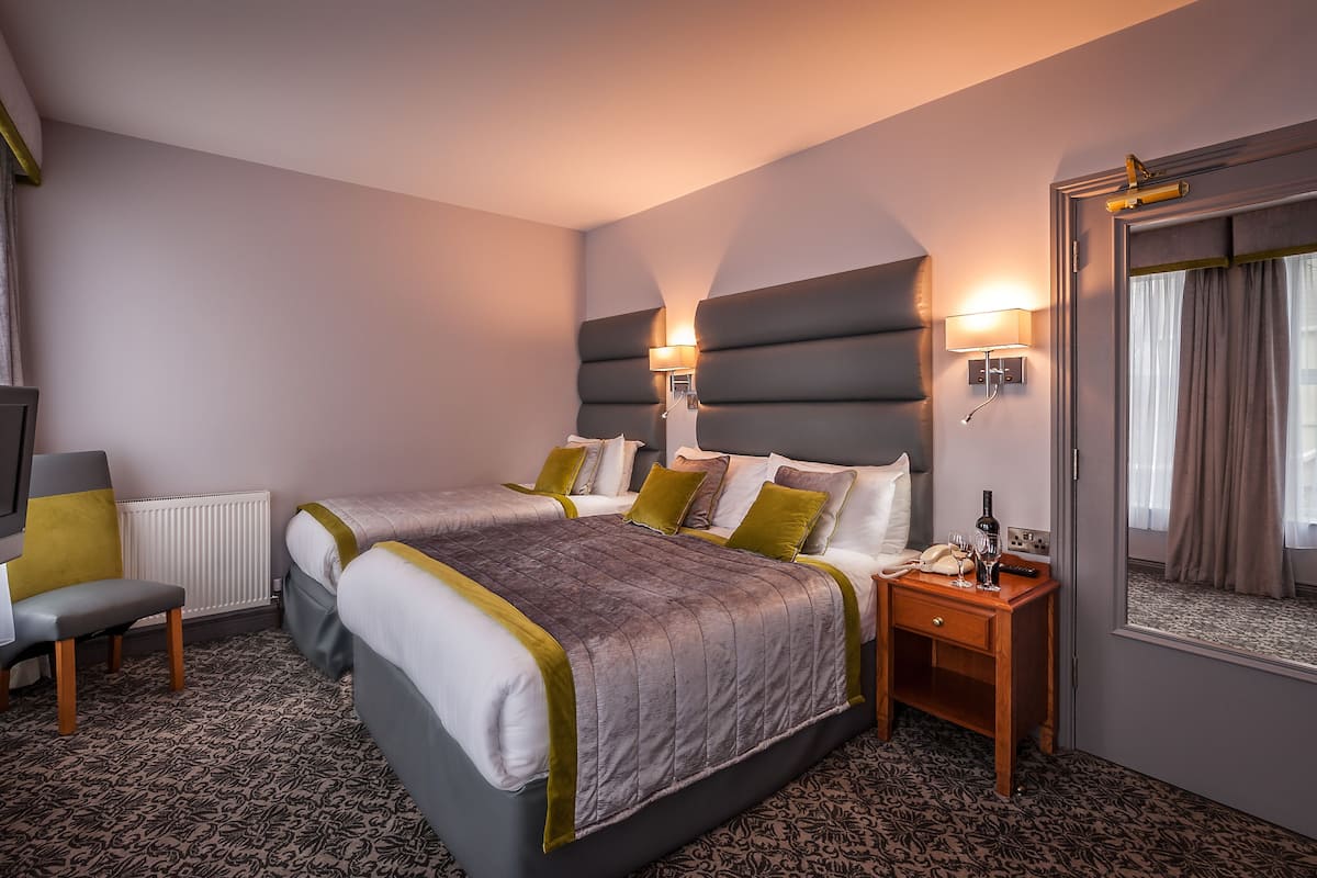 A hotel room with a large bed, two bedside tables, a chair, a TV, and a window with curtains.