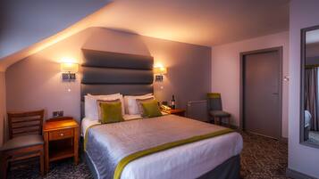 Una habitación de hotel con una cama grande, dos mesitas de noche, una silla, un escritorio y una puerta.