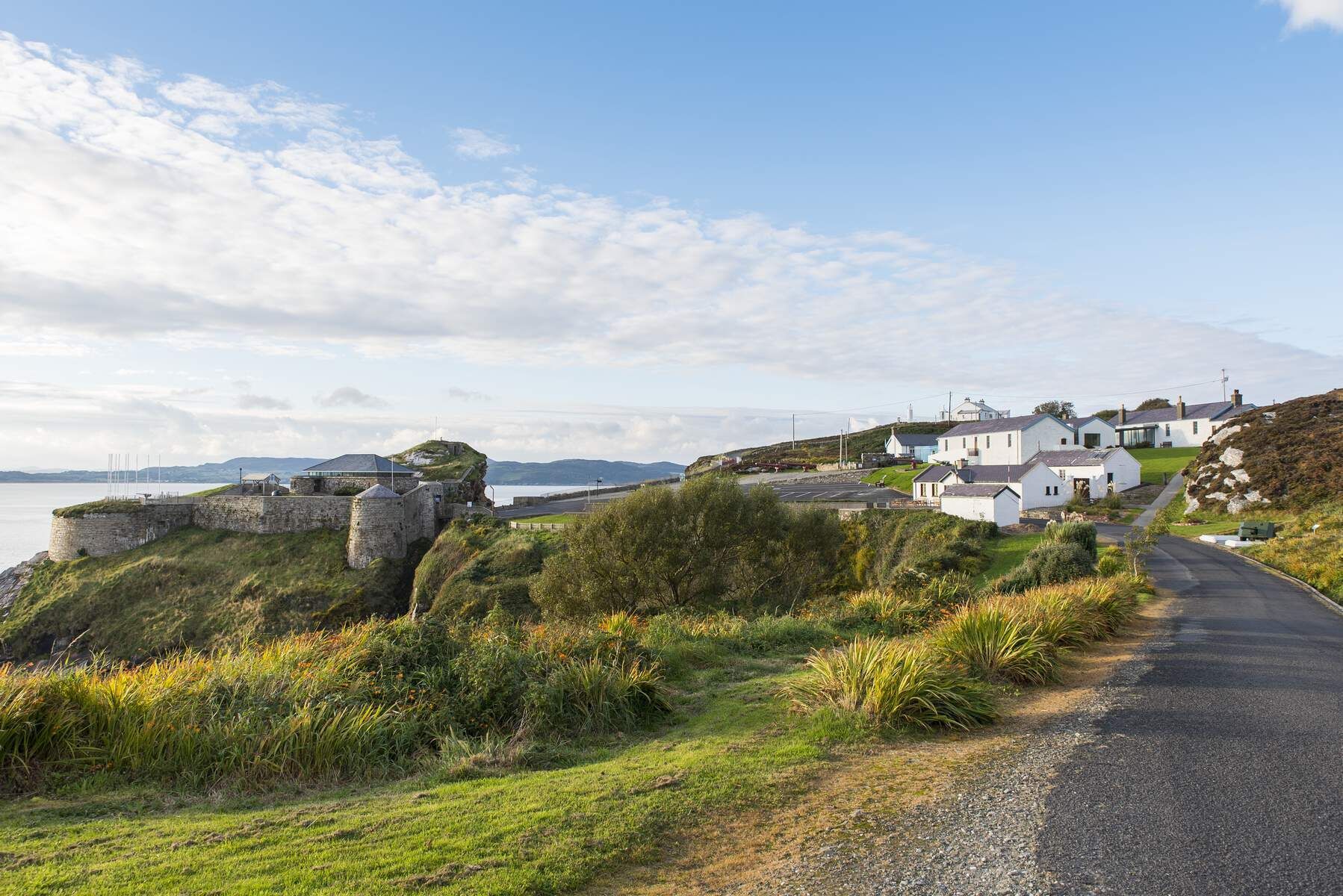 A coastal village with stone walls, white houses, and a road leading to the sea.