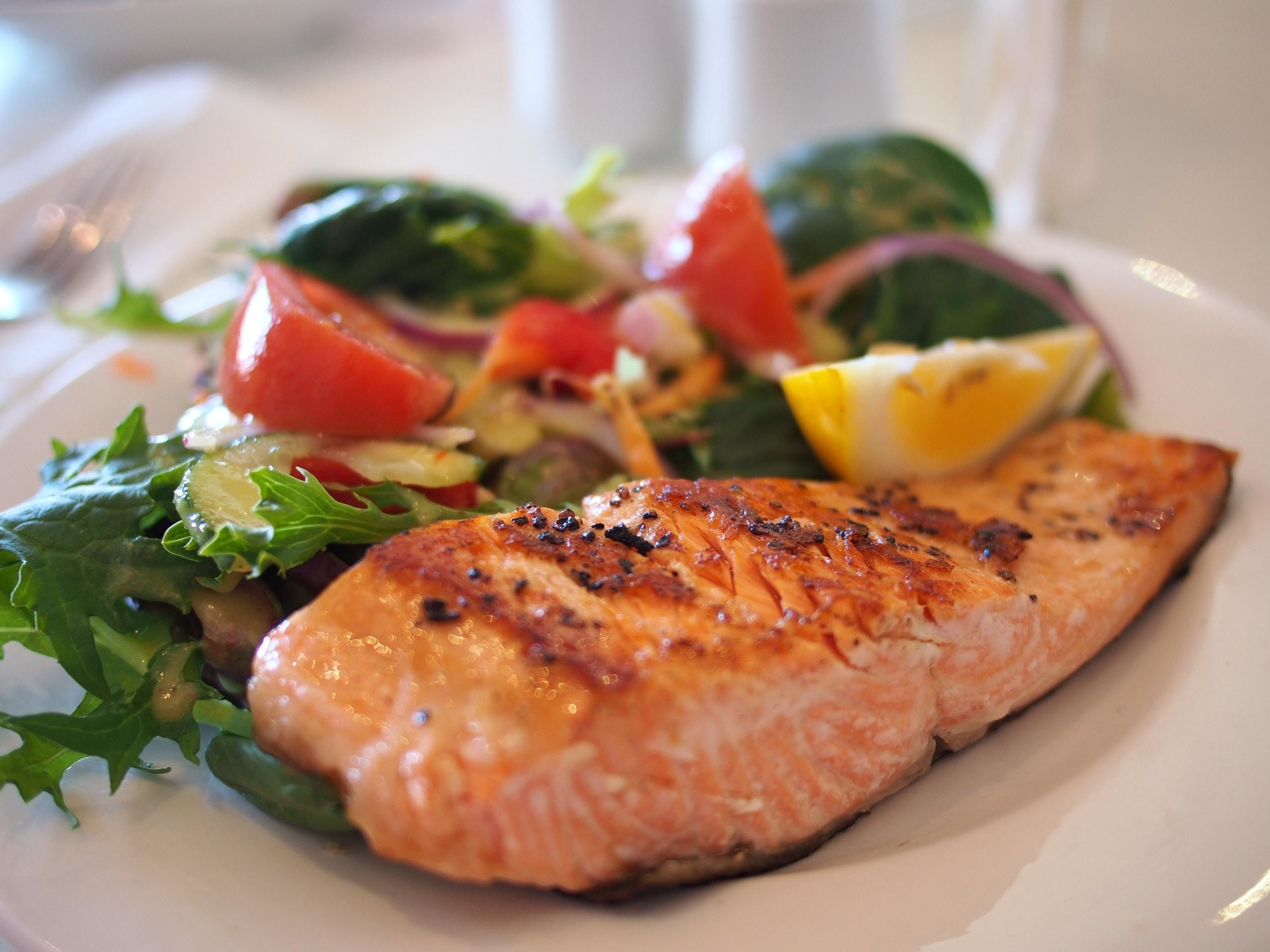 A plate with grilled salmon, a salad, and lemon slices.