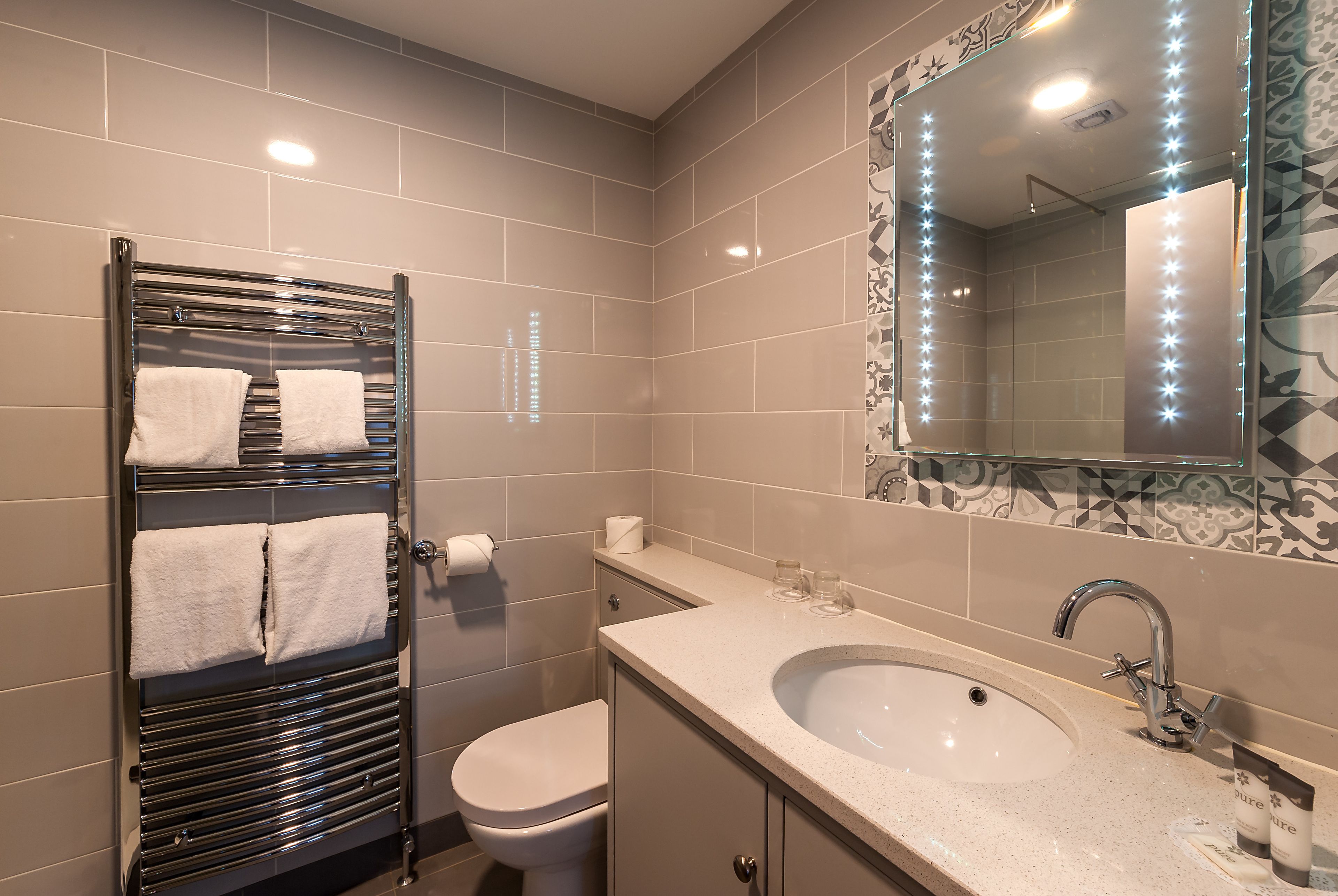 A modern bathroom with a glass shower enclosure, a white toilet, a sink with a mirror, and a towel rack with two towels.