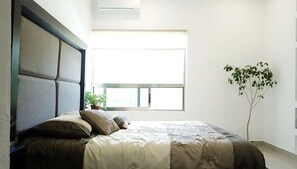A bedroom with a bed, a window, and a potted plant.
