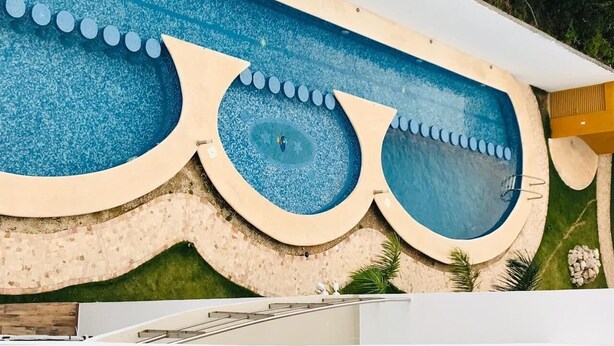 A swimming pool with a unique design, surrounded by a tiled deck and greenery. - Apartamento 1 (Cancun)