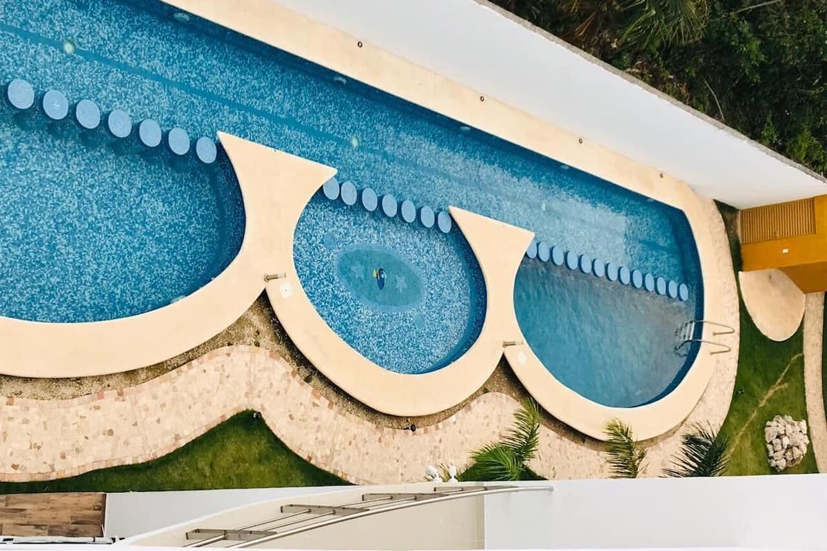 A swimming pool with a unique design, surrounded by a tiled deck and greenery.