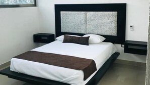 A modern bedroom with a large bed, a ceiling fan, an air conditioning unit, and a window with a view of trees. - Apartamento 1 (Cancun)