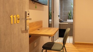 A modern room with a wooden desk, a chair, a flat-screen TV mounted on the wall, and a bathroom visible through an open door. - 574 Hotel (Medellín)