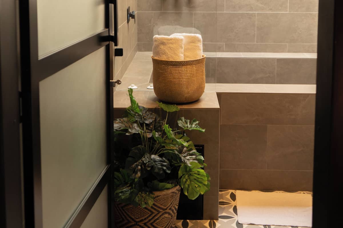 A modern bathroom with a skylight, a bathtub, a sink with toiletries, and a potted plant.