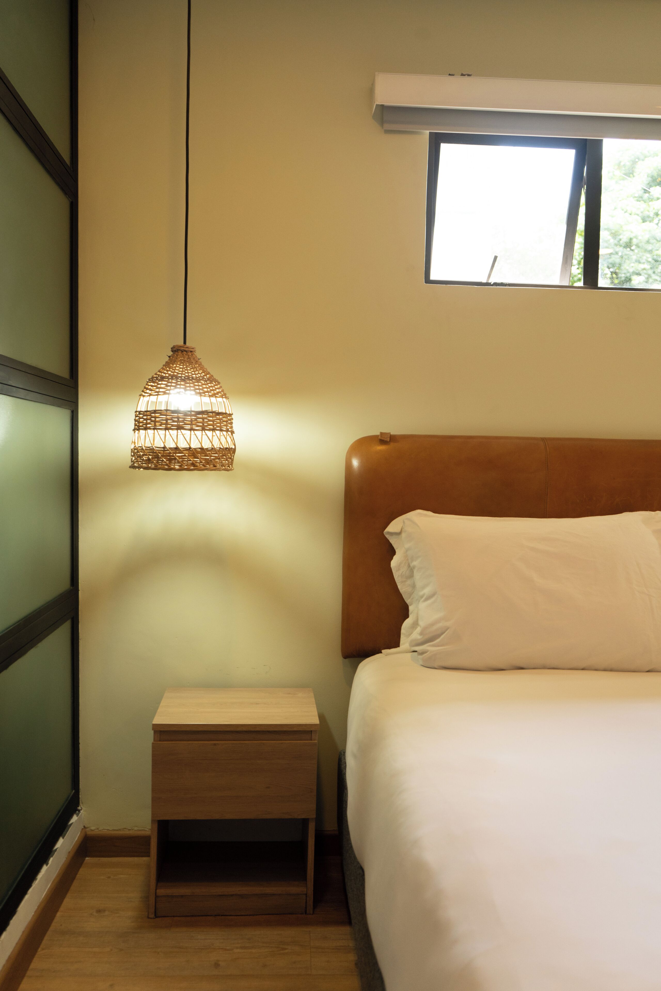 Ein Schlafzimmer mit Bett, Nachttisch, Pendelleuchte und Fenster.